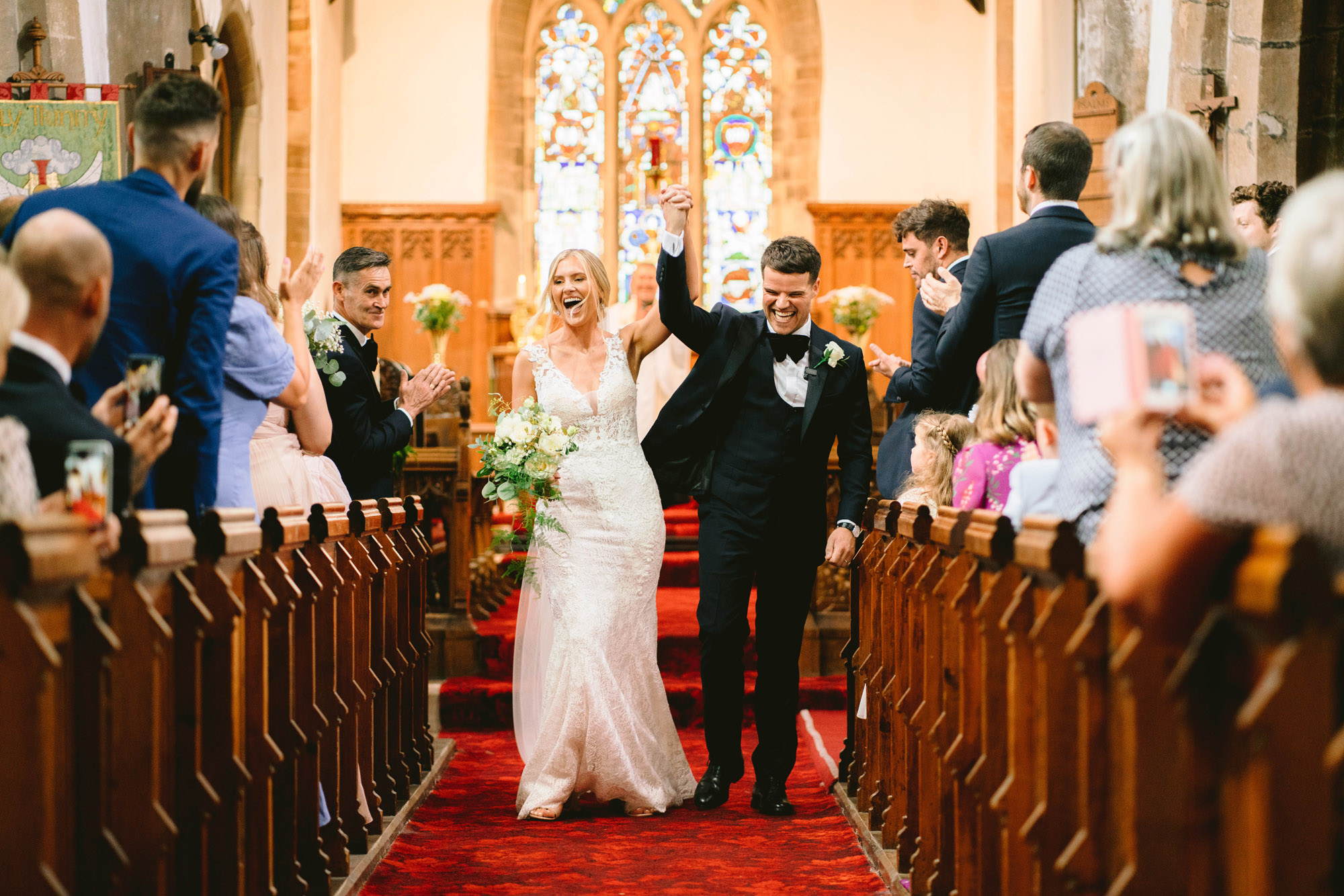 bride and groom wit fists in the air as they walk down the aisle after getting married in church before going to saltmarshe hall