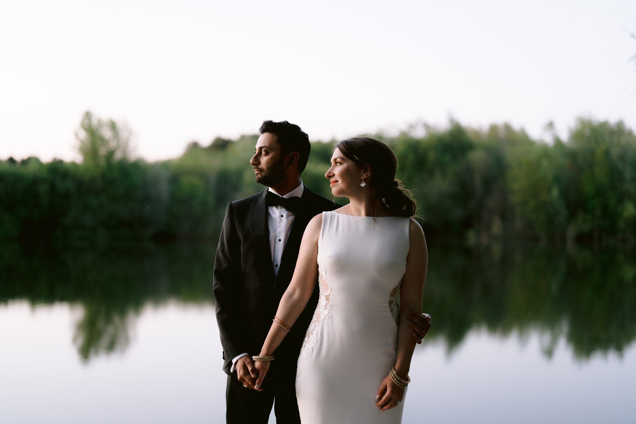hindu wedding couple by the lake at nunsmere hall groom is wearing tuxedo and bride a white dress